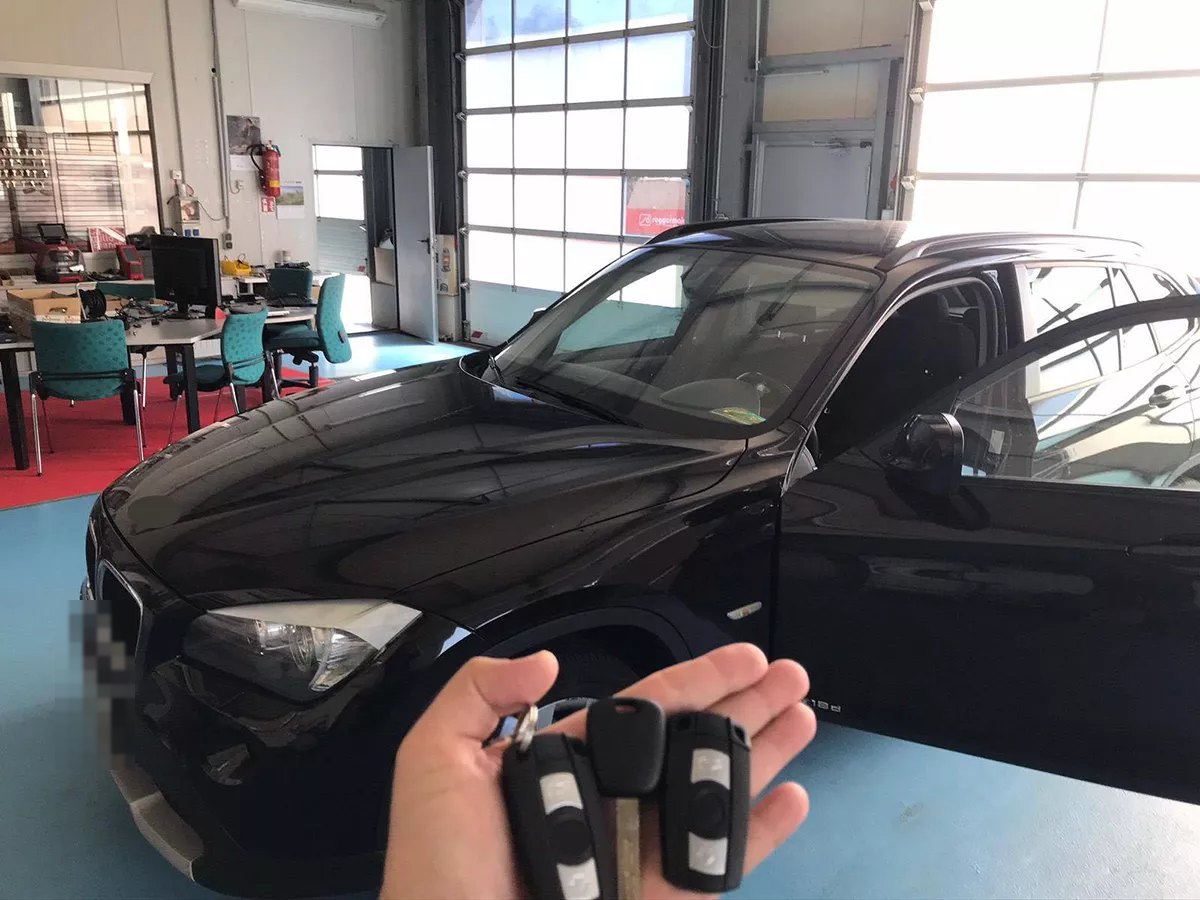 Three car keys held in a hand in front of a black BMW in the workshop